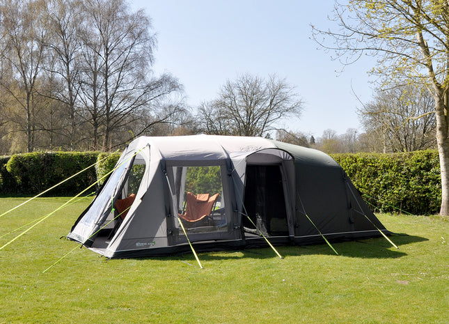 Gray camping tent with attached porch on a grassy area with trees in the background