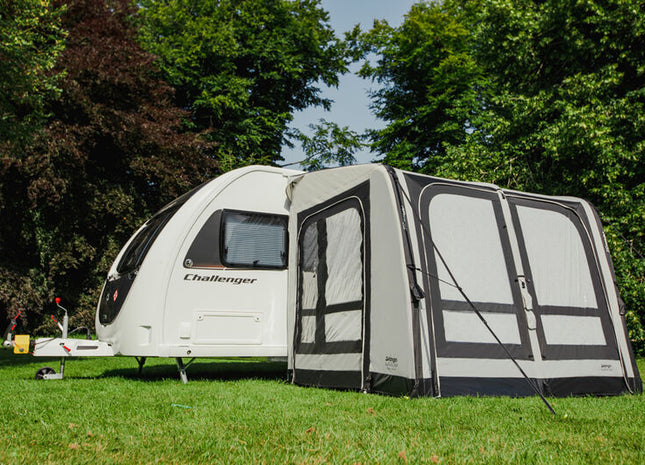Caravan with an attached awning on a grassy area with trees in the background