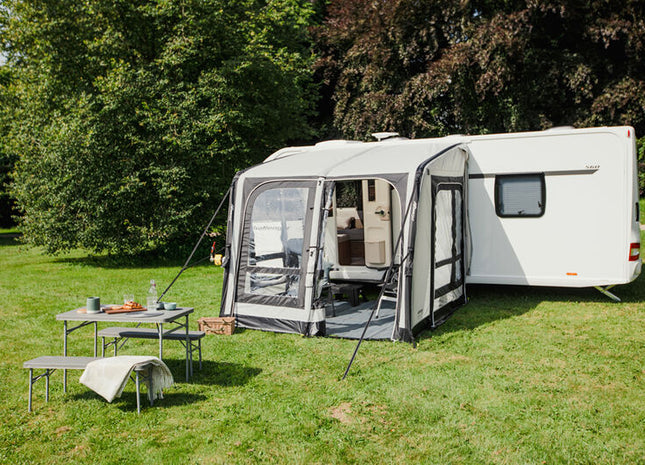Caravan with an awning extended on a grassy area with trees in the background