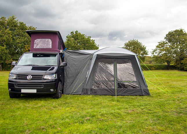 Van with a large gray awning extended on a grassy field with trees in the background