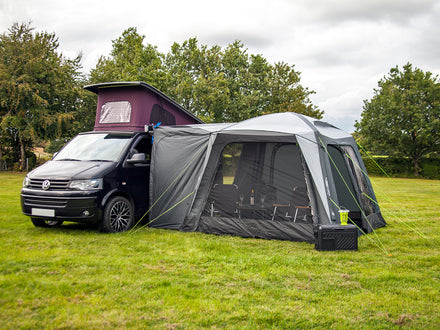 Van with a large gray inflatable tent attached in an outdoor setting with trees in the background.
