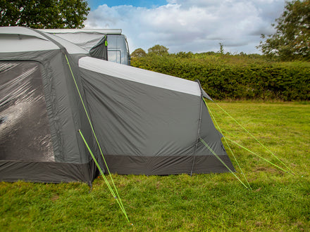 Gray camping tent with a flysheet on a grassy field with trees in the background