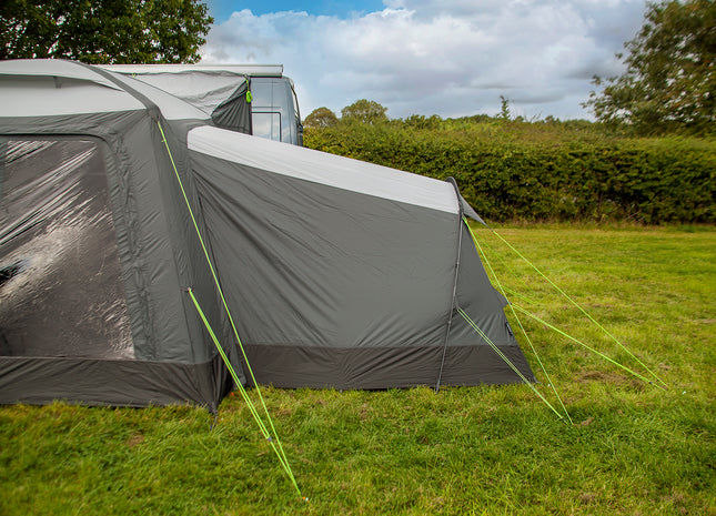 Gray camping tent with a flysheet on a grassy field with trees in the background