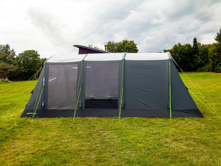 Camping tent with attached screen porch on a grassy field with trees in the background