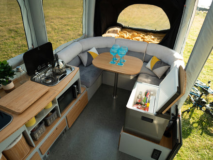 Interior of a compact camper van with kitchenette, dining area, and refrigerator.