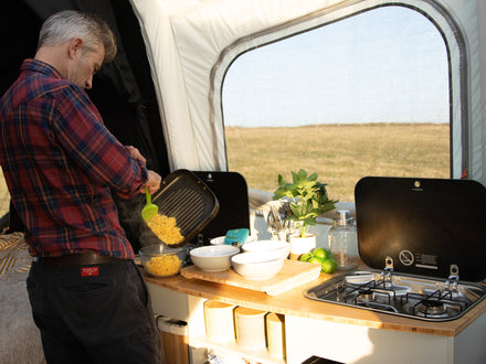 Man preparing food in a campervan kitchen with a scenic view outside.