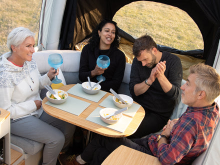 Four people sitting inside a camper van, enjoying a meal together.