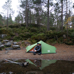 Person sitting inside a green tent in a forest setting