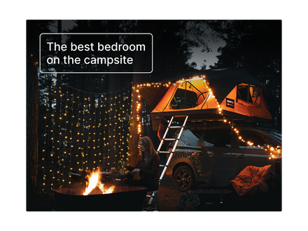A dark outdoor campsite scene at night with a person sitting near a fire pit, warm string lights, a rooftop tent on a camper van, and a text overlay that reads 'The best bedroom on the campsite'.