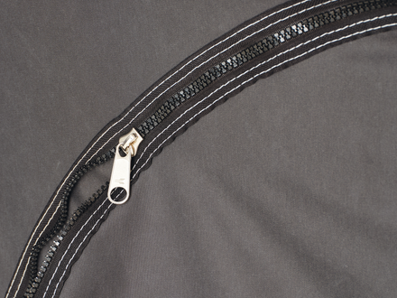 Close-up of a black zipper with white stitching on a gray background
