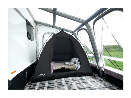 A black VANGO pop-up tent set up inside the open rear compartment of a white caravan, with a sleeping bag and pillow inside.