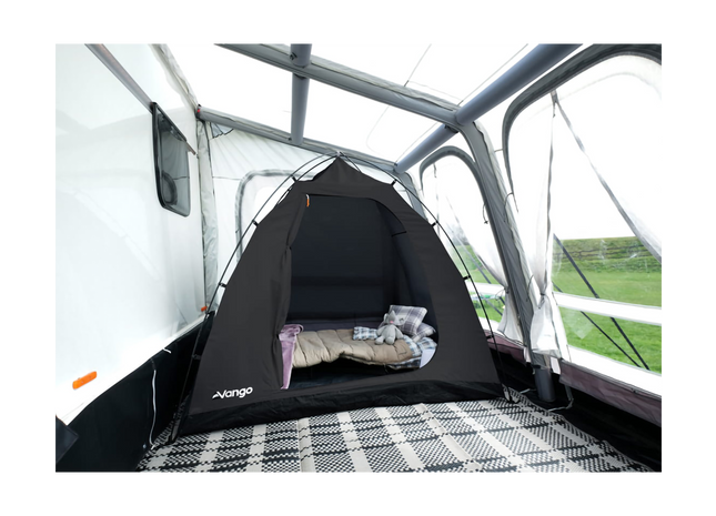 A black VANGO pop-up tent set up inside the open rear compartment of a white caravan, with a sleeping bag and pillow inside.