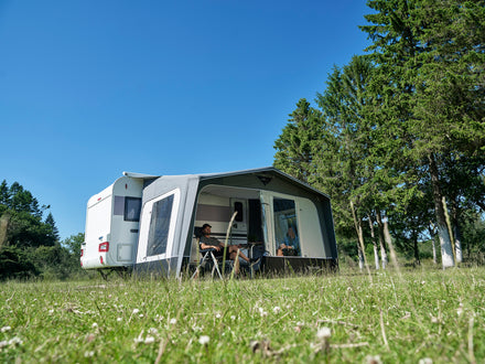 Camper van with an attached awning in a grassy area with trees