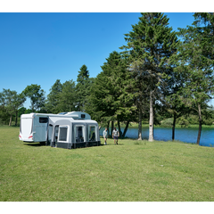 caravan with attached awning on a grassy area near a body of water with trees in the background.