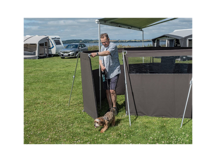 Man setting up a camping awning with a dog in a grassy area with other campers in the background.