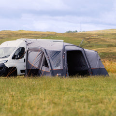 Van with a large gray awning extended in a grassy field with hills in the background