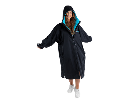 A woman wearing a black hooded changing robe with a bright turquoise lining, standing against a solid white background.