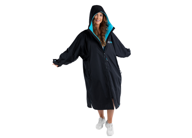 A woman wearing a black hooded changing robe with a bright turquoise lining, standing against a solid white background.