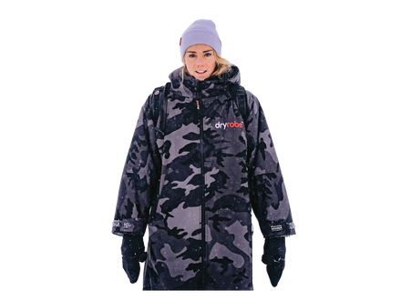A woman wearing a dark gray and black camouflage changing robe , a light purple beanie, and black gloves, shown against a plain white background.