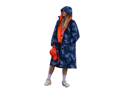 A model wearing a blue and gray camouflage hooded changing robe with a bright orange lining, holding an orange cap, set against a solid white background.
