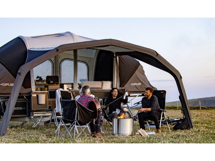 Family sitting under a large camping tent in a field with a scenic background