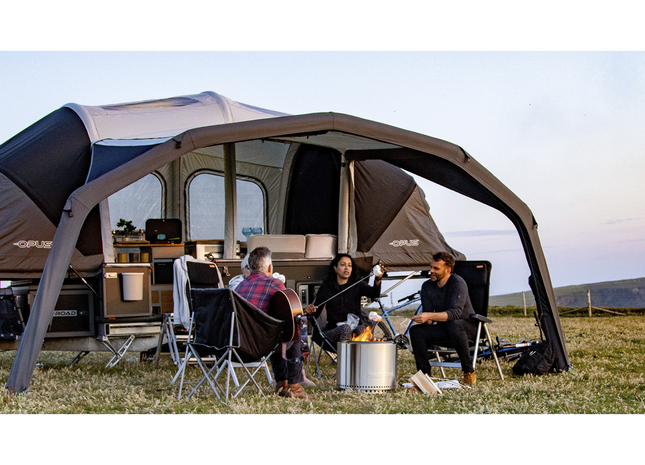 Family sitting under a large camping tent in a field with a scenic background