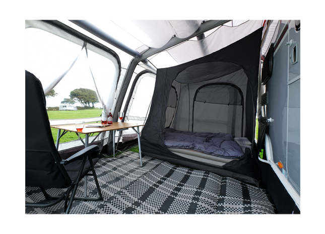 A black and gray pop-up camping canopy tent with an attached sleeping mesh enclosure, shown set up inside a vehicle camper shell. The interior features a black and white checkered floor mat, a black camping chair, and a small folding table.